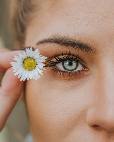 Woman wearing mascara while holding flower