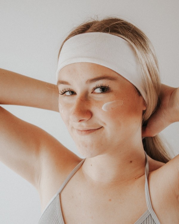 A woman smiles directly at the camera with a skin care product on her cheek.