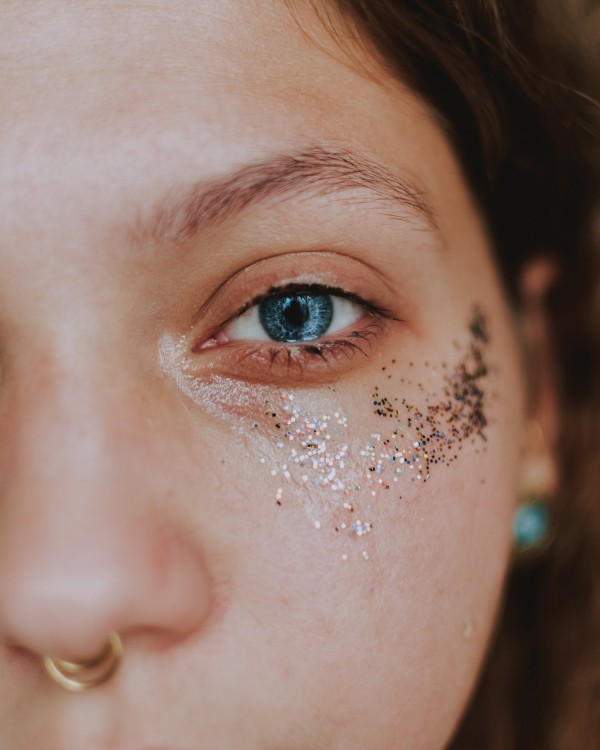 A girl with blue eyes and glitters on her face looks at the camera.