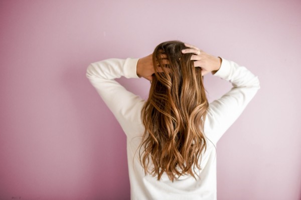 Woman in a white long sleeved shirt standing in front of pink wall.