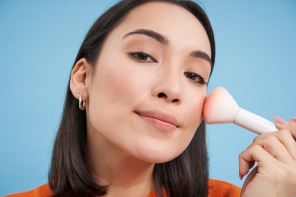 Asian woman applying blush makeup