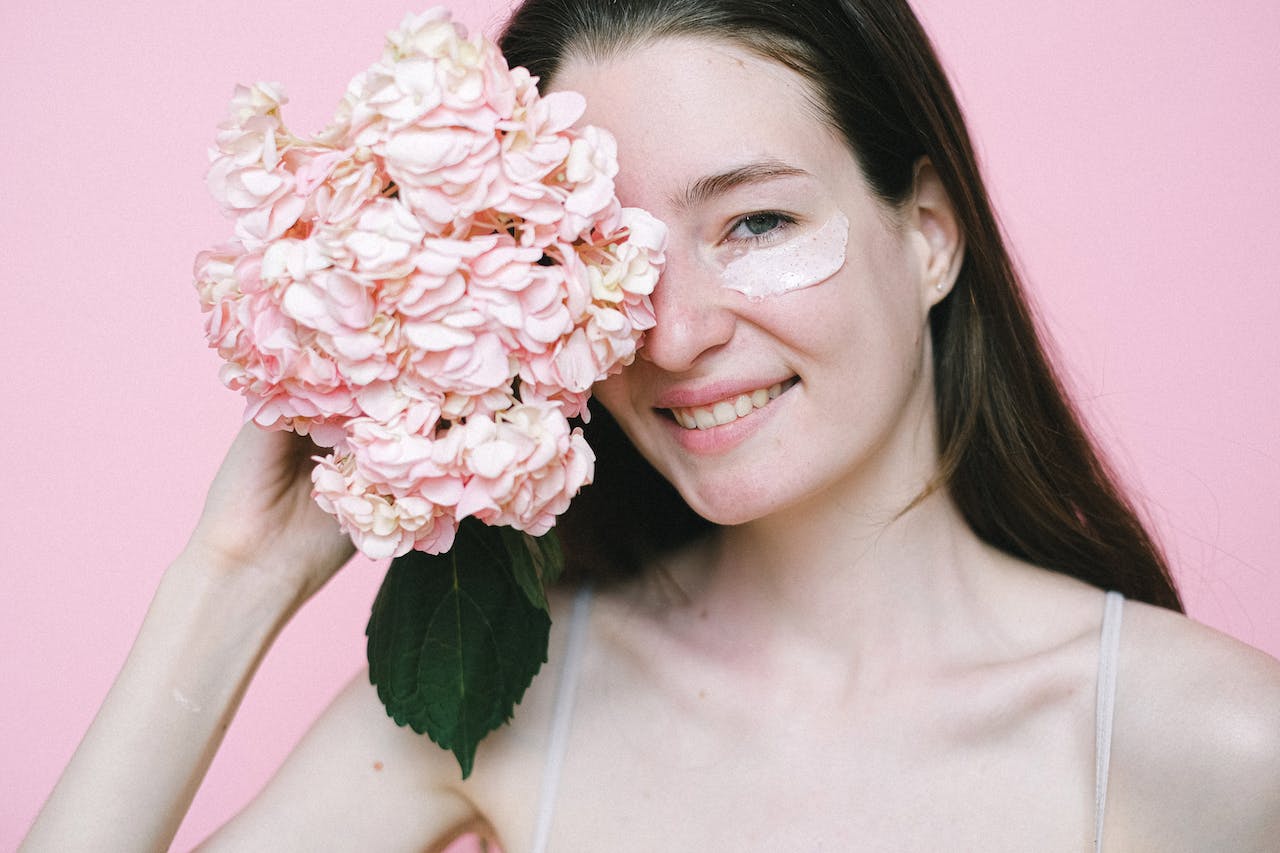 woman with eye cream holding pink flowers