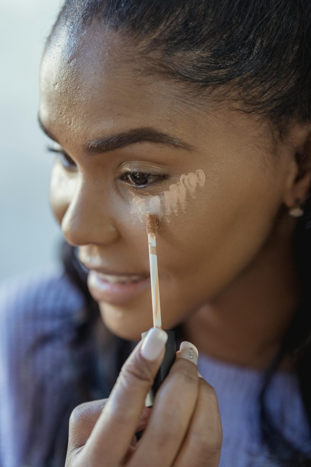 Black woman applying concealer or color corrector 
