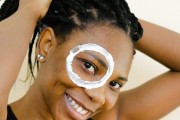 Black woman with lotion over eye fixing hair 